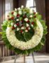 Corona fúnebre "Legado de Hildegarda" con rosas blancas y rojas, crisantemos blancos y follaje verde, en sala de velación pre