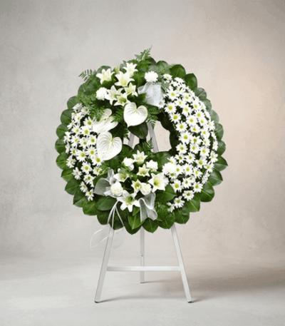 Corona fúnebre Legado de Paz con flores blancas, lirios, margaritas y anturios, sobre un caballete blanco en un fondo elegant