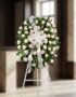 Corona fúnebre Serenidad con rosas blancas y follaje verde, lazo blanco, sobre un trípode en una sala de velación premium con