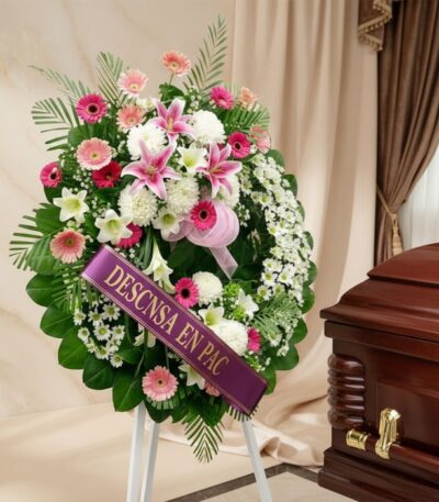 Imponente corona fúnebre "Homenaje a Mathias" con lirios blancos y rosados, gerberas y follaje verde, junto a un ataúd en sal