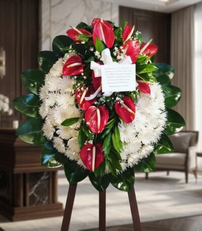 Corona fúnebre Trinidad con flores blancas y anturios rojos, en una sala de velación premium con luz natural suave.