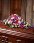 Cubre caja fúnebre "El Legado de Francisco" con flores variadas en tonos rosas, morados y blancos, sobre un ataúd de madera o