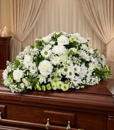 Cubre caja fúnebre Epifania con flores blancas sobre un ataúd de madera oscura, en un entorno elegante y sereno con iluminaci