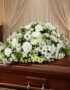 Cubre caja fúnebre Epifania con flores blancas sobre un ataúd de madera oscura, en un entorno elegante y sereno con iluminaci