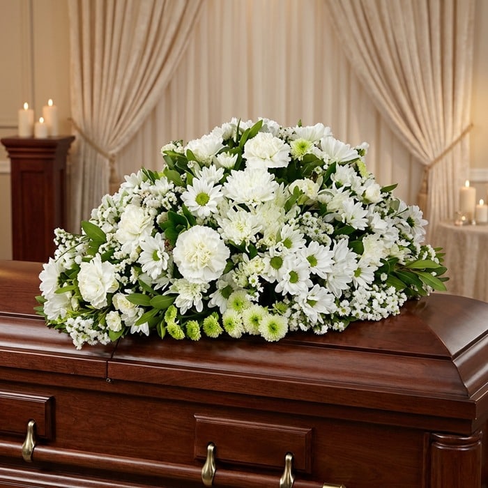 Cubre caja fúnebre Epifania con flores blancas sobre un ataúd de madera oscura, en un entorno elegante y sereno con iluminaci