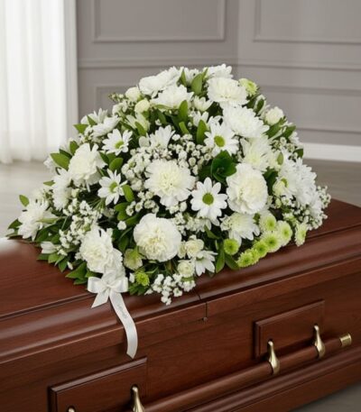 Cubre caja fúnebre Epifania con flores blancas y cinta de condolencia, vista desde un ángulo diferente y composición renovada