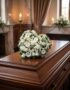 Elegante cubre caja fúnebre con rosas blancas y margaritas, formando un corazón sobre un ataúd de madera oscura en un entorno