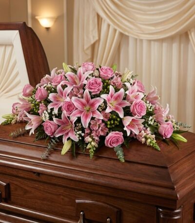 Cubre caja fúnebre Ifigenia con rosas y lirios rosados, eucalipto y follaje verde, elegantemente dispuesto sobre un ataúd de