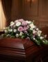 Cubre caja fúnebre "Jardín de Ines" con rosas lilas, margaritas blancas y flores moradas sobre un ataúd de madera oscura en u