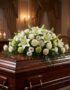 Cubre caja fúnebre 'Legado Eterno de Tomás' con lirios blancos, rosas y follaje verde sobre un ataúd de madera oscura en un a