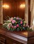 Cubre caja fúnebre 'Legado Sereno de Ivon' con rosas rosadas, claveles y cardos azules sobre un ataúd de madera oscura en un