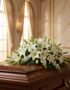 Cubre caja fúnebre 'Legado de José' con rosas blancas y lirios, sobre un ataúd de madera oscura en un entorno elegante y sole