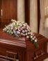 Cubre caja fúnebre elegante con rosas rosadas y follaje verde, delicadamente dispuesto sobre un ataúd de madera oscura en un