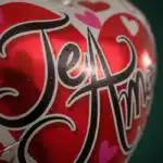Primer plano extremo de un globo metalizado rojo y blanco con la frase 'Te Amo' en negro, cubierto de sutiles gotas de rocío