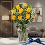 Jarrón de cristal con doce rosas amarillas frescas y gypsophila, sobre una mesa de mármol con un lazo azul marino, en un ambi