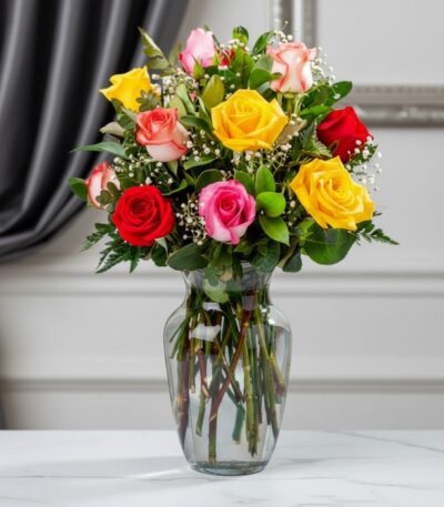 Jarrón de cristal transparente con un ramo de 12 rosas de colores variados: rojas, amarillas, rosas y blancas, con follaje ve