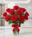 Jarrón de cristal con 18 rosas rojas vibrantes y abiertas, adornado con un elegante moño rojo, sobre una superficie de mármol