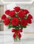 Jarrón de cristal con 18 rosas rojas vibrantes y abiertas, adornado con un elegante moño rojo, sobre una superficie de mármol