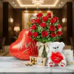 Jarrón Dulce Amor con rosas rojas, un oso de peluche blanco, chocolates Ferrero Rocher y un globo de 'I Love You' sobre mármo