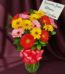 Jarrón de cristal con un vibrante arreglo de gerberas multicolores (rojas, amarillas, rosas) y follaje verde, atado con un la