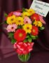 Jarrón de cristal con un vibrante arreglo de gerberas multicolores (rojas, amarillas, rosas) y follaje verde, atado con un la