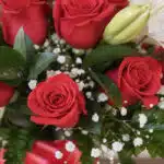Primer plano extremo de un arreglo floral 'Jarrón Otoño' con rosas rojas vibrantes, lirios blancos y follaje verde, con sutil