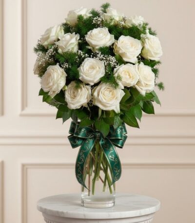 Jarrón Pétalos Blancos con un arreglo floral de rosas blancas abiertas, follaje verde y un moño verde elegante, sobre una sup