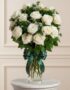 Jarrón Pétalos Blancos con un arreglo floral de rosas blancas abiertas, follaje verde y un moño verde elegante, sobre una sup