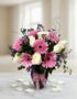 Jarrón Primavera con un elegante arreglo floral de rosas blancas, gerberas rosas y pequeñas flores moradas, sobre una mesa de