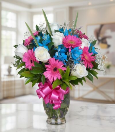 Jarrón Primavera con un arreglo floral vibrante de rosas blancas, gerberas fucsia y alstroemerias azules, sobre una superfici