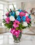 Jarrón Primavera con un arreglo floral vibrante de rosas blancas, gerberas fucsia y alstroemerias azules, sobre una superfici