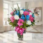 Jarrón Primavera con rosas blancas, gerberas fucsia y alstroemerias azules, sobre una mesa de mármol en un ambiente luminoso