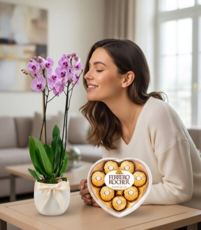 Mujer sonriendo y oliendo una orquídea GALA morada en maceta blanca con lazo, junto a una caja de chocolates Ferrero Rocher e