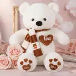 Oso de felpa blanco con bufanda a rayas marrones y blancas, corazón bordado 'LOVE' y patas con huellas de corazón, rodeado de