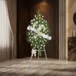 Pedestal conmemorativo Legado de Marcos con arreglo floral fúnebre blanco, lirios y rosas, en sala de velación elegante con i