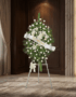 Pedestal conmemorativo Legado de Marcos con arreglo floral fúnebre blanco, lirios y rosas, en sala de velación elegante con i