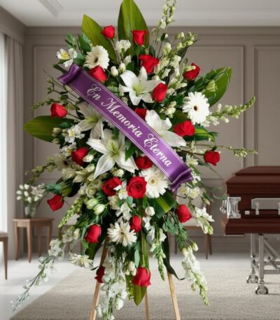 Pedestal fúnebre Adoración con rosas rojas, lirios blancos y margaritas, adornado con cinta morada 'En Memoria Eterna', junto