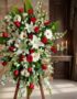 Pedestal fúnebre Adoración con rosas rojas, lirios blancos y margaritas, en sala de velación premium con luz natural suave.