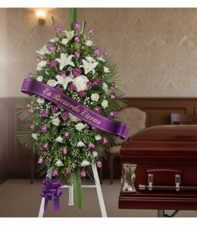 Pedestal fúnebre Esteban con rosas moradas y blancas, lirios, y cinta 'En Recuerdo Eterno' junto a un ataúd en sala de velaci