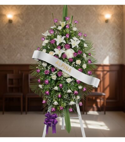 Pedestal fúnebre Esteban con arreglo floral de lirios blancos, rosas moradas y follaje verde, banda blanca con nombre 'Esteba