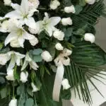 Fotografía macro premium del Pedestal Fúnebre Eternidad, mostrando lirios blancos, rosas crema y follaje verde con rocío suti