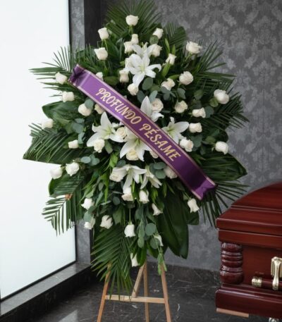 Pedestal fúnebre Eternidad con rosas blancas, lirios y follaje verde, adornado con una cinta morada que dice 'Profundo Pésame
