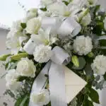 Fotografía macro premium del Pedestal Fúnebre Hasta Pronto, mostrando texturas hiperrealistas de pétalos blancos y follaje ve