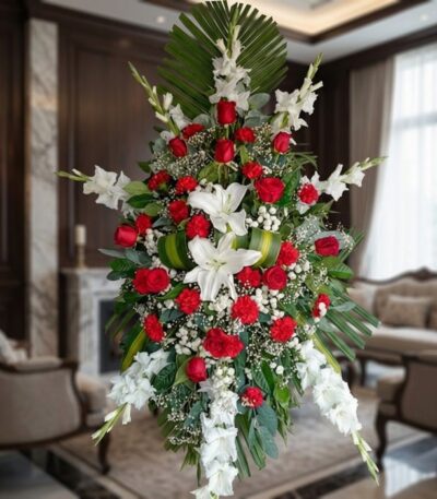 Pedestal fúnebre Homenaje con rosas rojas, lirios blancos y gladiolos, en una sala de velación premium con luz natural suave.