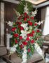 Pedestal fúnebre Homenaje con rosas rojas, lirios blancos y gladiolos, en una sala de velación premium con luz natural suave.