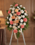 Pedestal fúnebre de homenaje para Timoteo, con arreglo floral de claveles coral, rosas durazno y crisantemos blancos, en sala