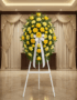Pedestal fúnebre Legado Sereno con rosas y claveles amarillos, lazo blanco, en sala de velación elegante con cortinas y luz c
