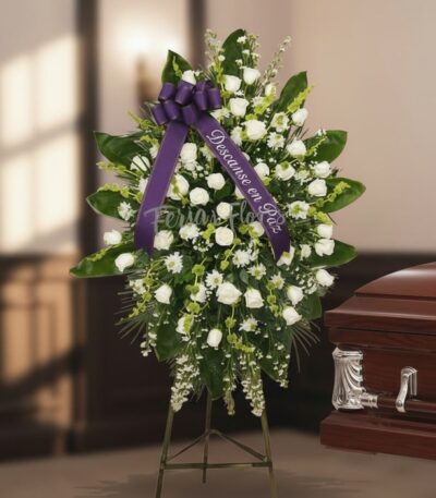 Pedestal fúnebre "Nunca te Olvidaré" con rosas blancas y follaje verde, cinta morada con mensaje de condolencia, junto a un a