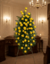 Pedestal fúnebre alto con rosas amarillas vibrantes y follaje verde, presentado en una elegante sala de velación con iluminac