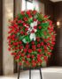 Pedestal fúnebre de rosas rojas intensas y follaje verde, con un lazo blanco, en una sala de velación premium con luz natural